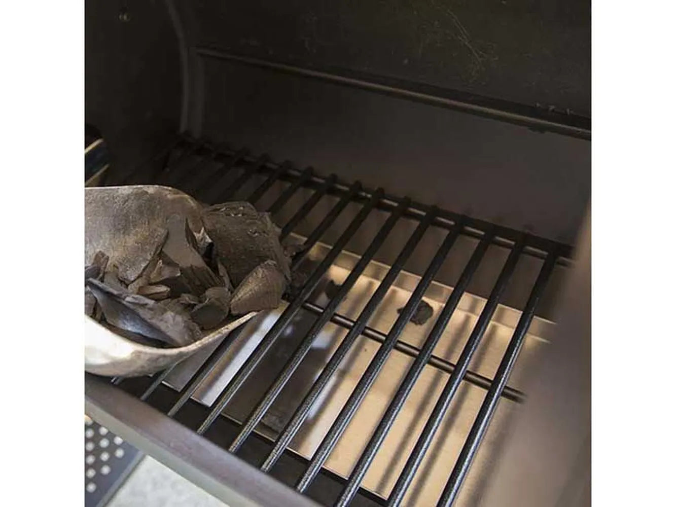 Close-up of the side firebox interior with charcoal being added to the grate inside the Broil King Regal Charcoal Offset 400 smoker grill.