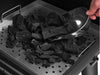 Metal scoop pouring lump charcoal into the charcoal tray of the Broil King Regal Charcoal Offset 500 smoker grill.