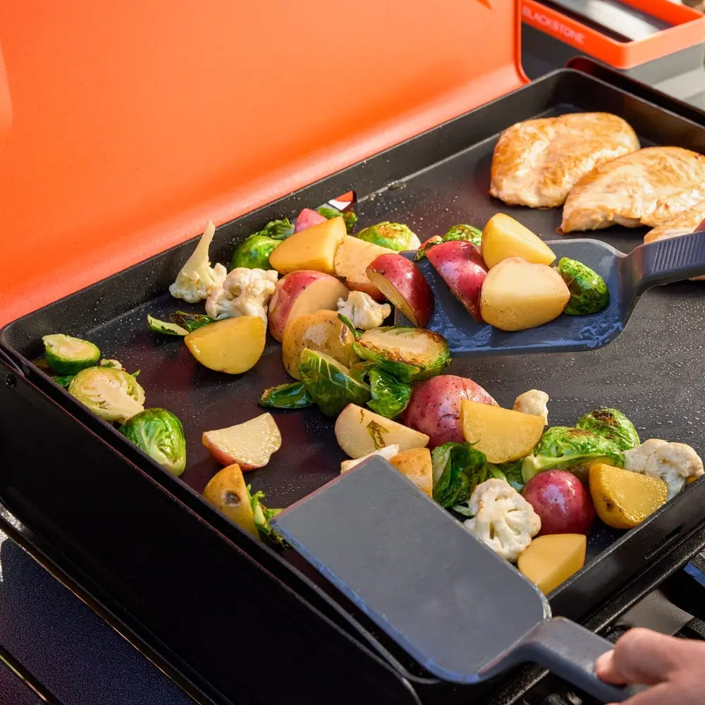 Close-up view of grilled vegetables and chicken cooking on the Blackstone ceramic-coated griddle plate, highlighting even sear and space efficiency.