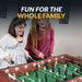 An image titled "Fun For The Whole Family" showing two young women smiling and playing with the Hathaway Metropolitan 54-inch Foosball Table in a game room setting.