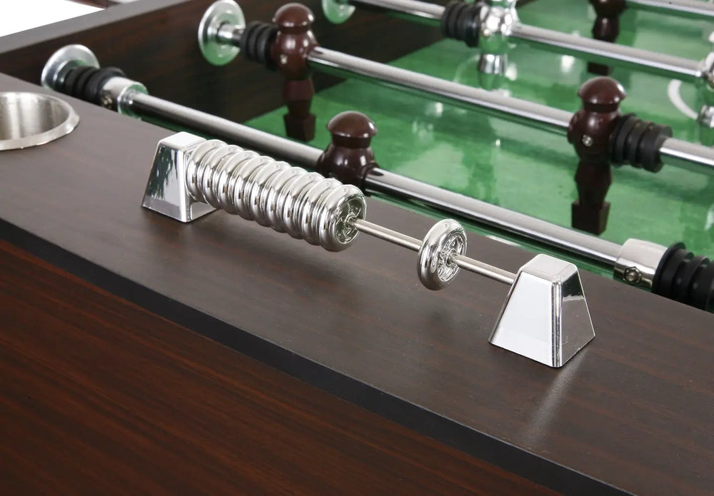 Close-up of shiny chrome score counter on a dark wood foosball table, with metallic foosball player figures and rods in the background.