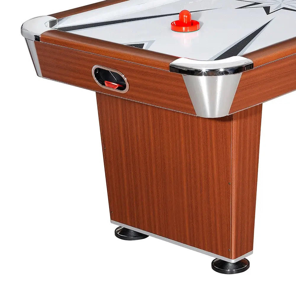 Side view of one corner of the air hockey table showing the wood grain finish, chrome corner protector, red pusher on the playfield, and puck return slot built into the side panel.