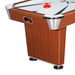 Side view of one corner of the air hockey table showing the wood grain finish, chrome corner protector, red pusher on the playfield, and puck return slot built into the side panel.