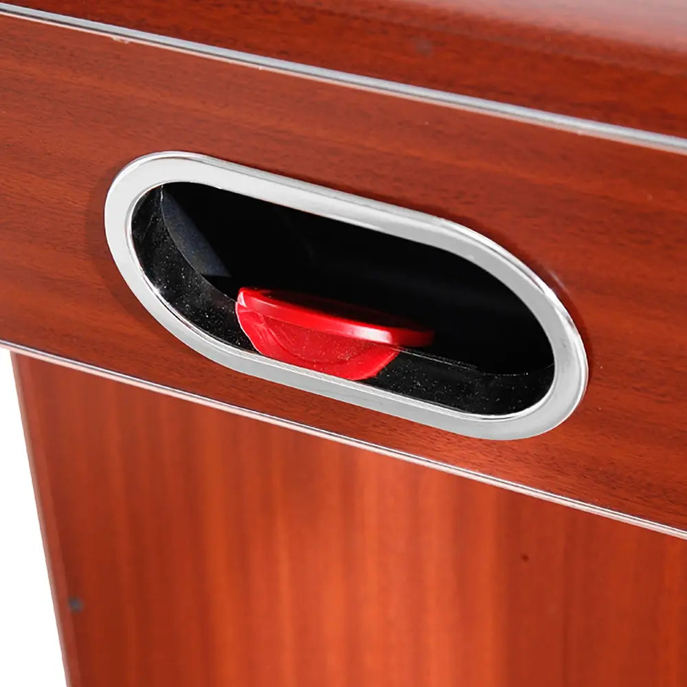 Close-up of the puck return slot on the air hockey table’s wood-paneled side, containing a red puck. Chrome trim outlines the slot for visual contrast.