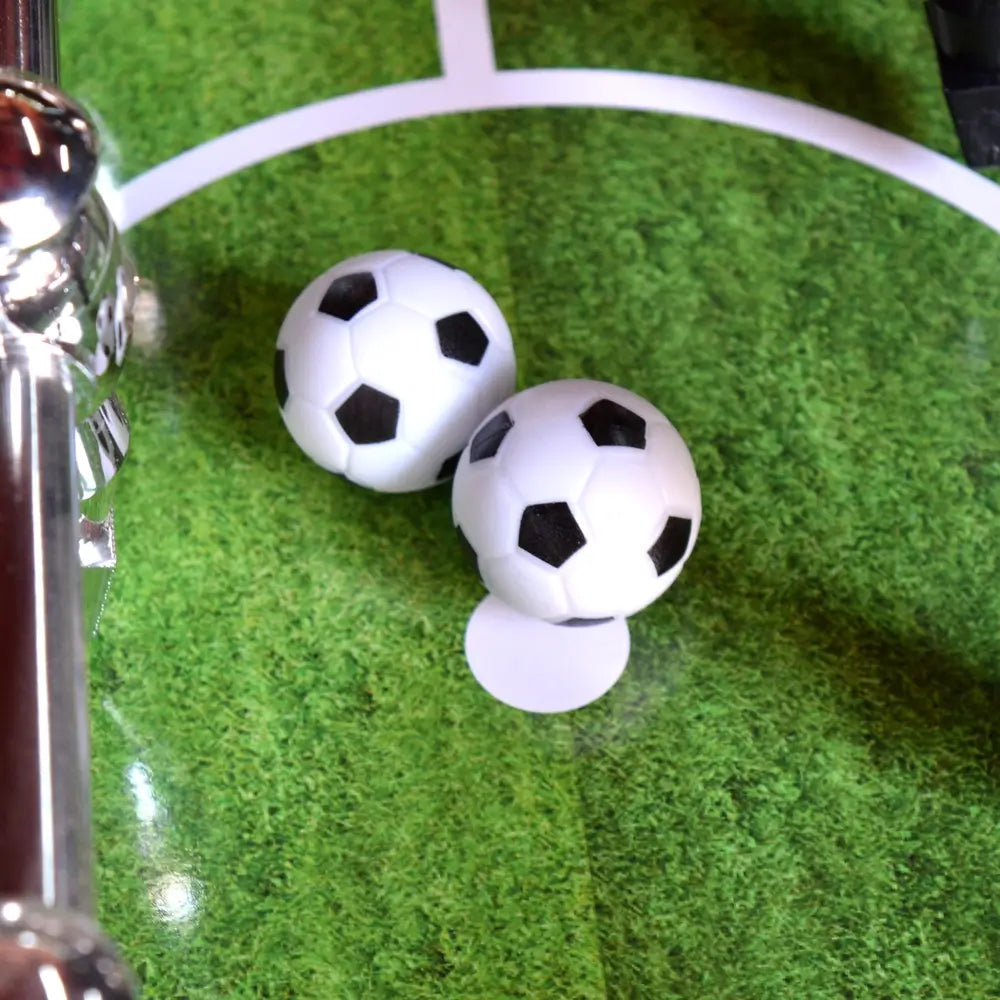 Two black-and-white 36-mm foosballs resting on the green playfield near the center circle of the table.