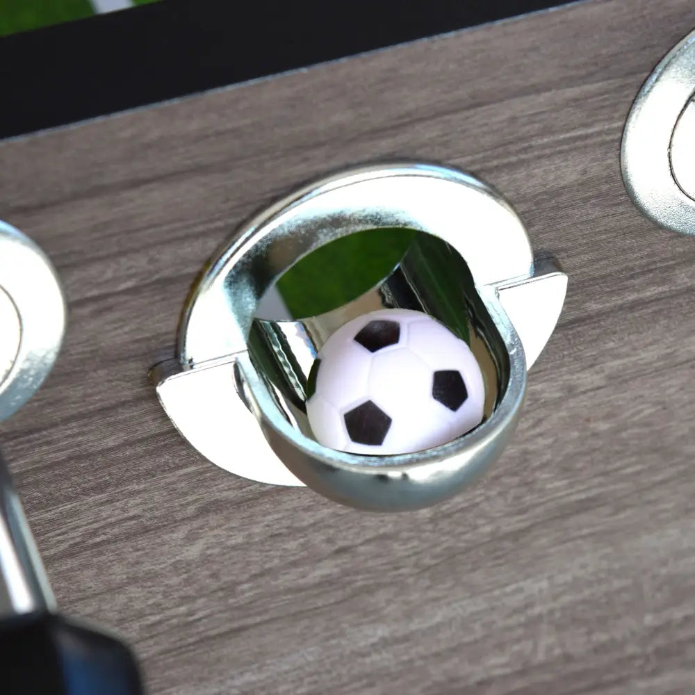 Chrome ball entry cup embedded in the driftwood table surface with a foosball inside, ready for gameplay.