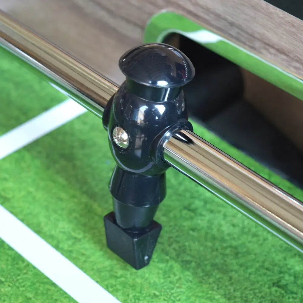 Close-up of a black ABS-molded foosball player on a chrome rod, mounted on the green playfield of the Hathaway Driftwood foosball table.