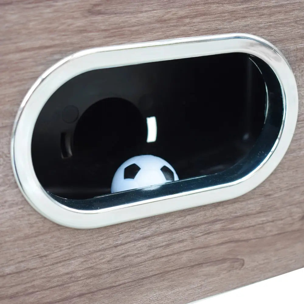 Close-up of the ball return slot on the Hathaway Driftwood foosball table, with a white and black foosball visible inside.