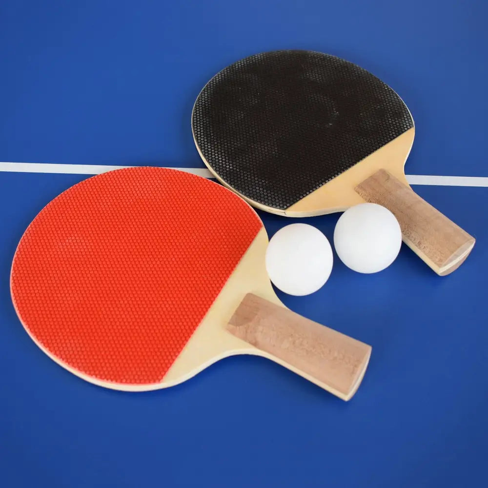 Close-up of table tennis paddles with red and black rubber faces and two white ping pong balls, placed on blue playing surface.