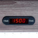 Digital game timer with red LED display embedded in wood grain table, showing 15-minute countdown for game sessions.
