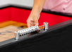 Close-up of hand using the chrome abacus-style scorekeeper on a black shuffleboard table with red interior.