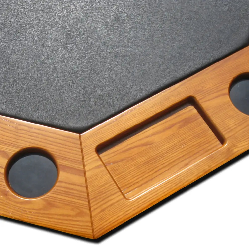 Close-up of Kingston poker table showing black faux leather surface with integrated wooden chip tray and drink holders in a honey oak finish.