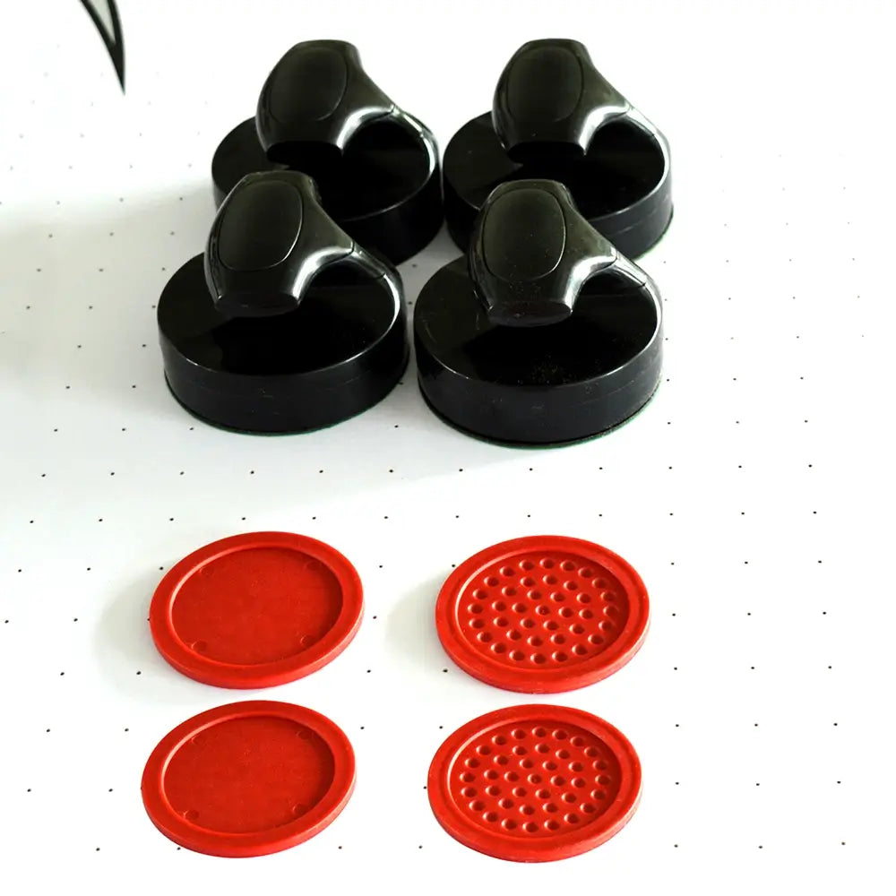 Close-up of air hockey accessories on playfield: four black ergonomic strikers and four red textured pucks for enhanced gameplay.