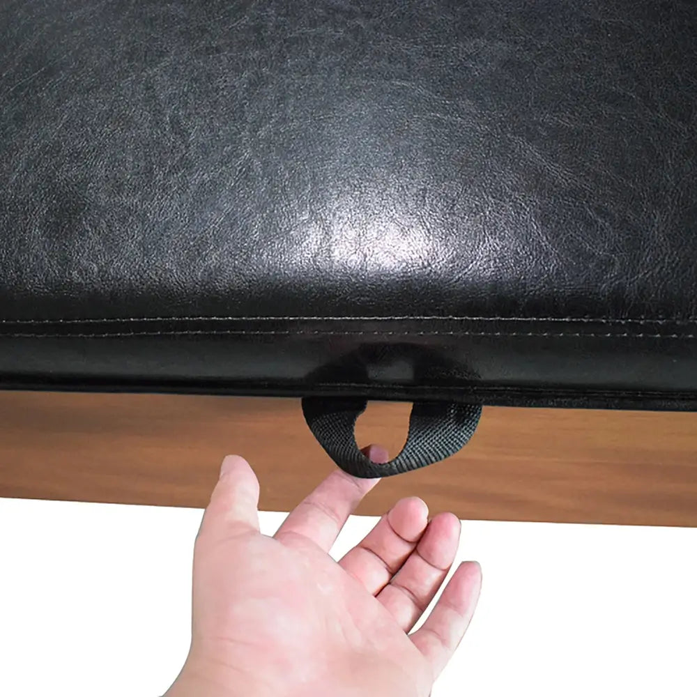 Hand lifting black faux leather storage bench seat using a fabric handle, part of multi-functional game table bench.
