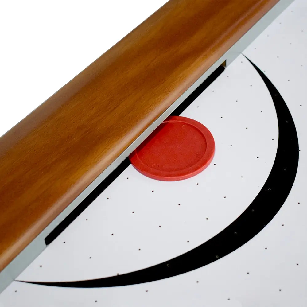 Air hockey puck near goal on smooth white playfield with black graphic lines, surrounded by rich wood-tone frame and side rails.