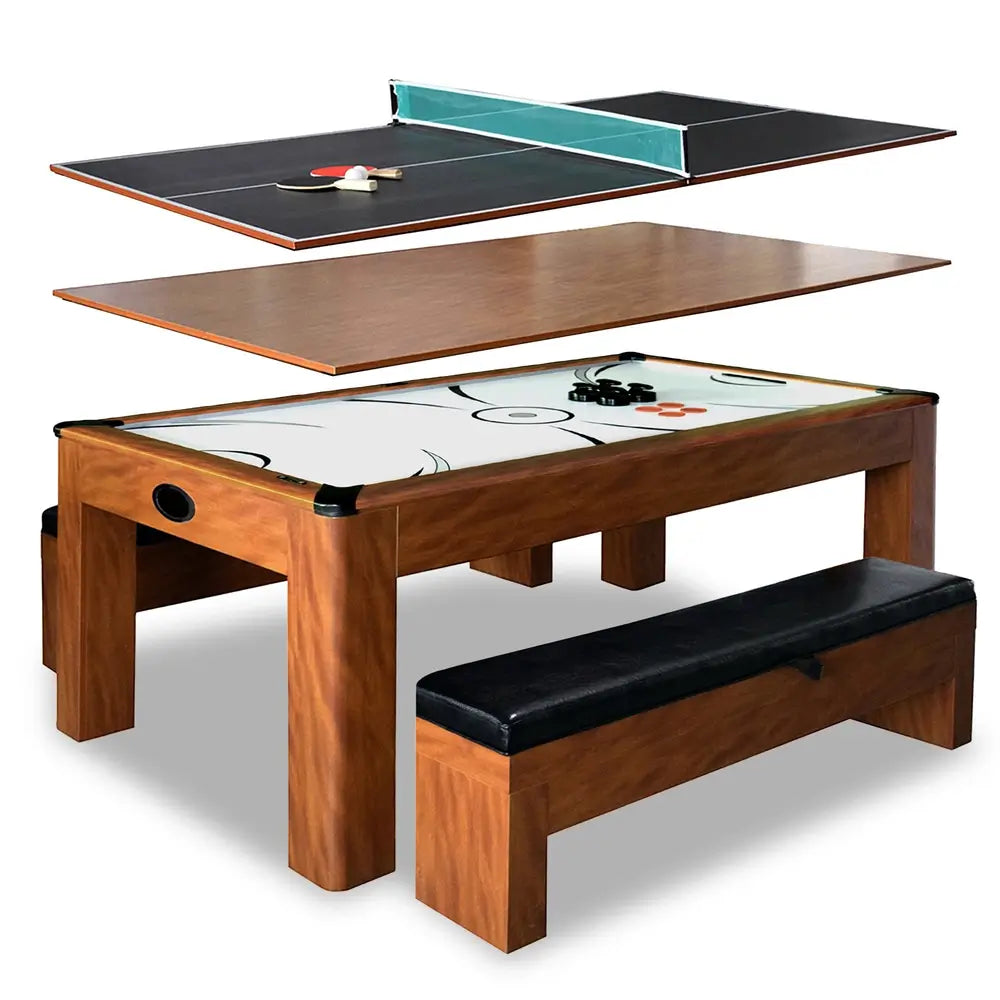 Exploded view of multi-functional game table showing removable tops for table tennis, dining, and air hockey; features cherry wood frame, white playfield, and black cushioned bench seating.