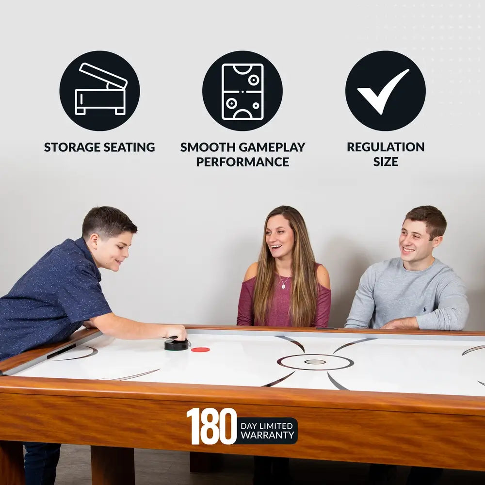 Boy playing air hockey on 7-ft table with two seated spectators; text highlights storage seating, regulation size, and smooth gameplay.