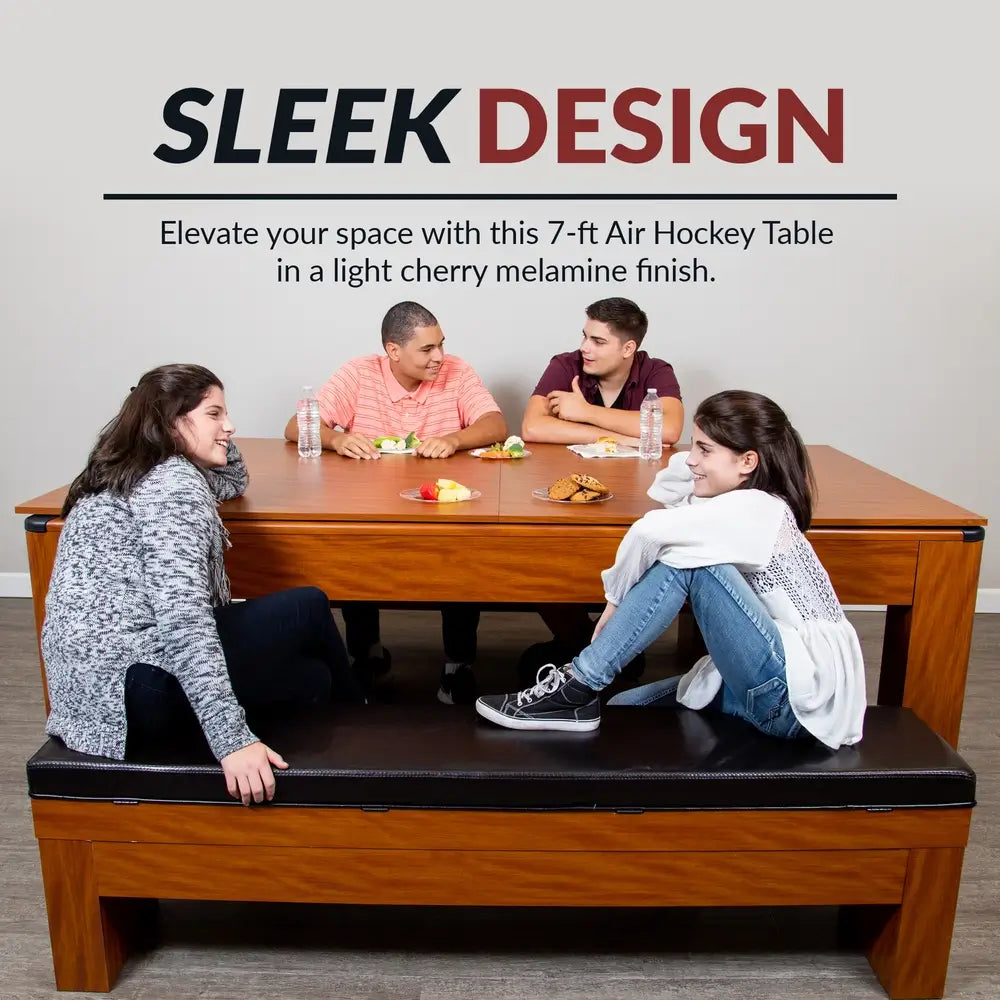 Family gathered around 7-ft convertible air hockey table with light cherry melamine finish, used as dining table with food and drinks.
