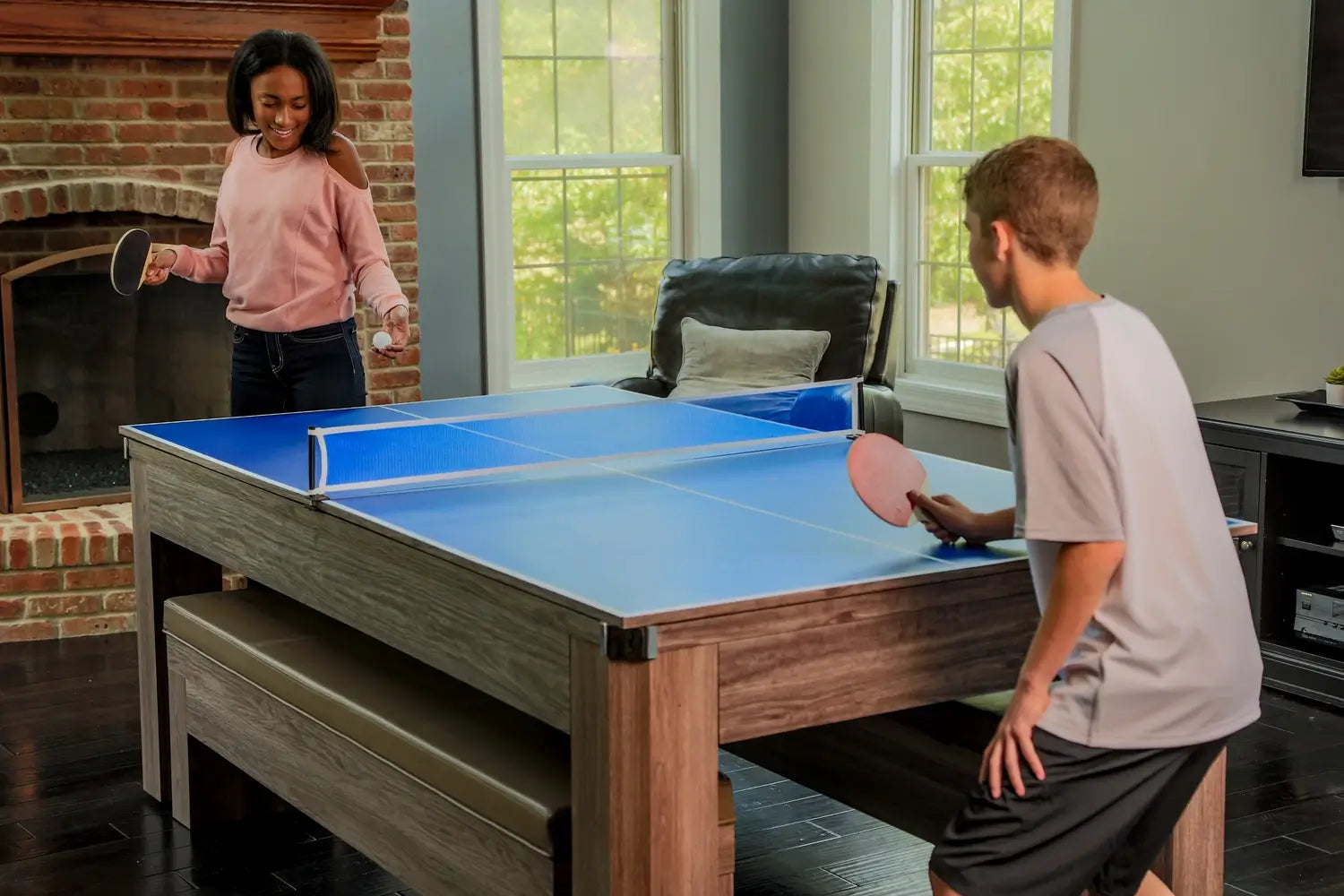 Two teenagers playing a friendly match of ping pong on the blue table tennis conversion top of the Hathaway Newport 3-in-1 game table.