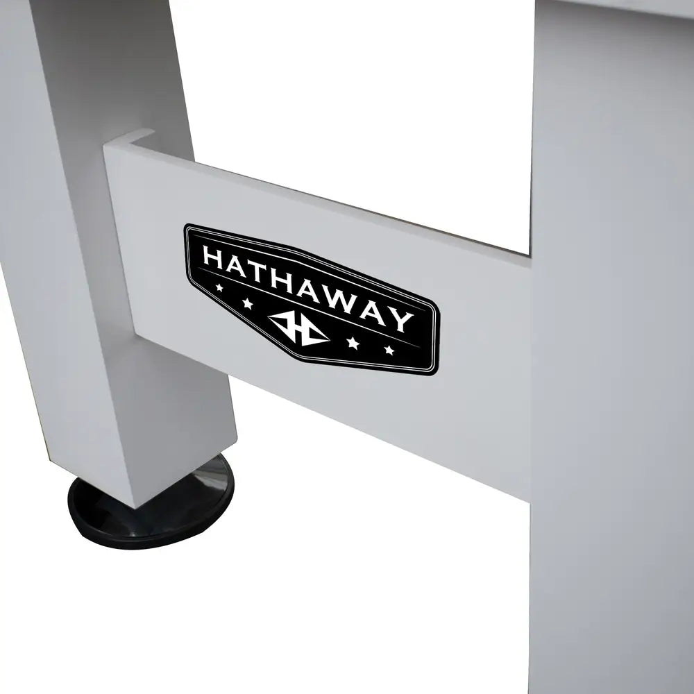 Close-up view of Hathaway logo plaque on the crossbeam of a white foosball table leg, showcasing durable branding on the frame.