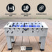 Foosball table placed on patio deck with icons promoting family fun, durability, and space versatility; includes 180-day limited warranty badge.