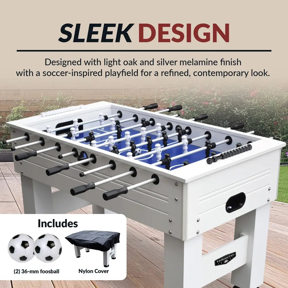 White and silver foosball table with soccer-style blue playfield set on backyard patio, includes two 36mm foosballs and protective nylon cover.