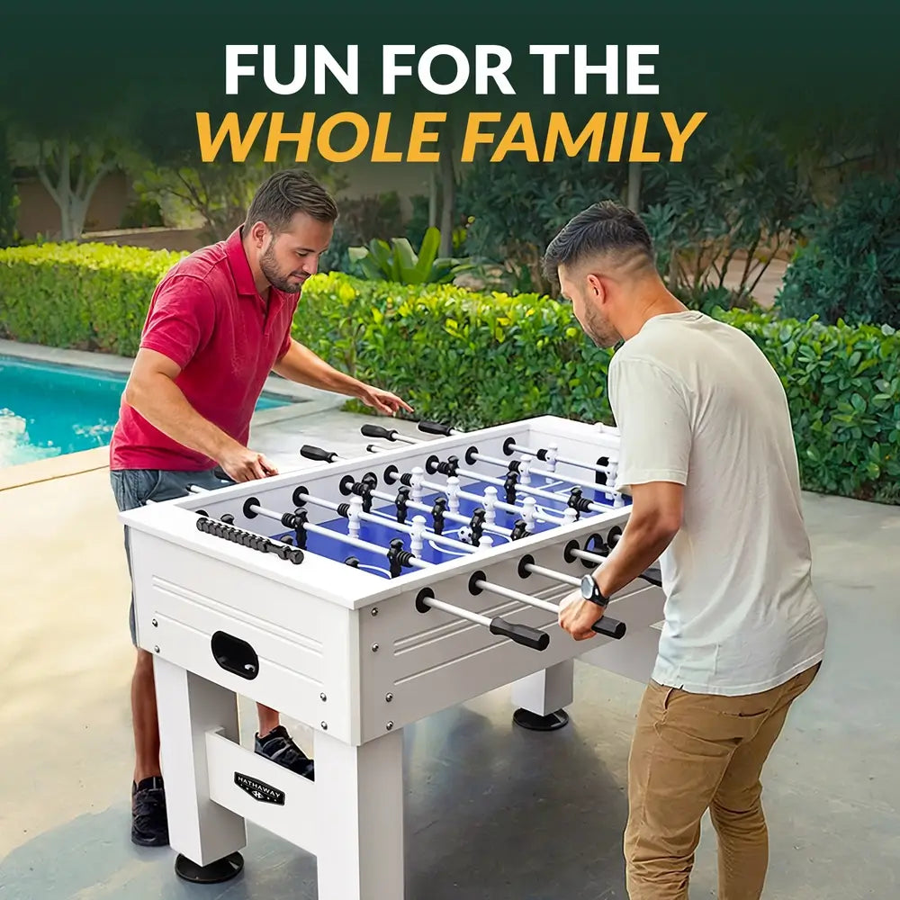 Two men enjoying a game of foosball on a white Hathaway table near a pool, showcasing outdoor fun and family-friendly entertainment.