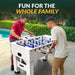 Two men enjoying a game of foosball on a white Hathaway table near a pool, showcasing outdoor fun and family-friendly entertainment.