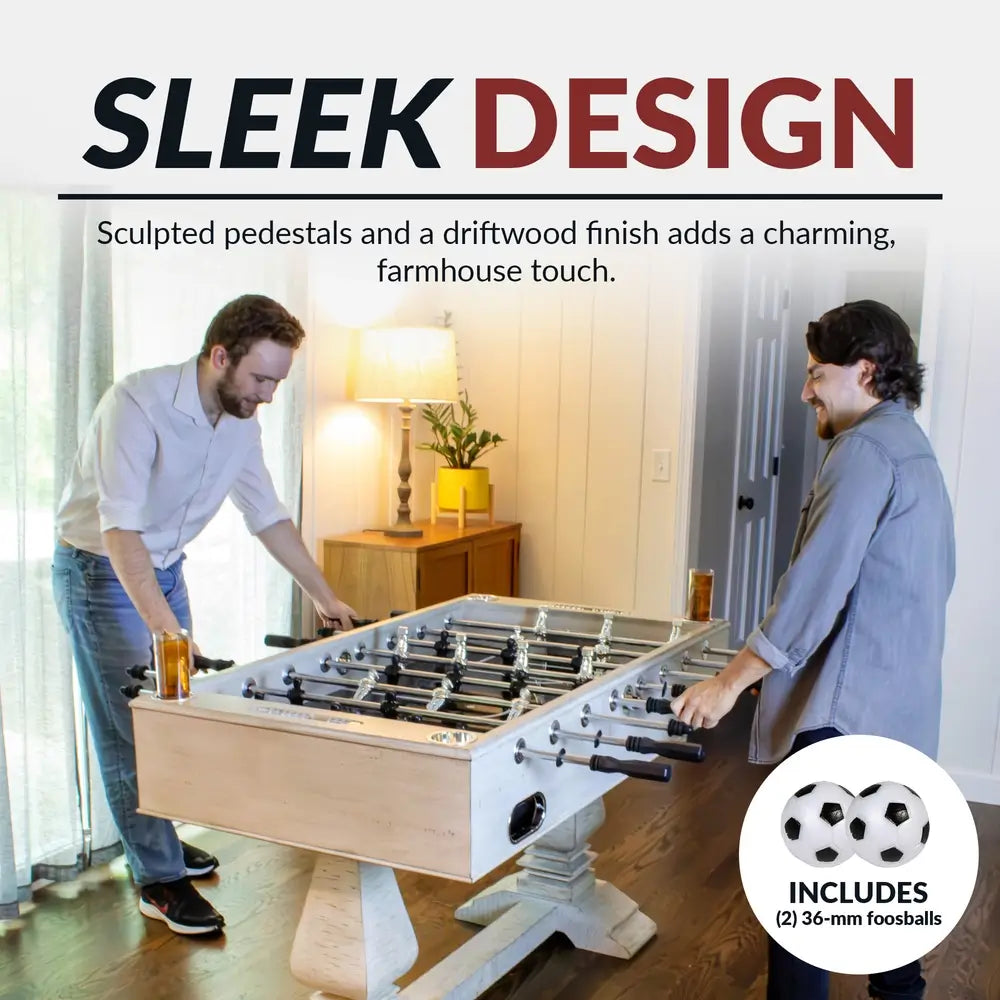 Two men playing foosball on a driftwood-finish farmhouse foosball table with sculpted pedestal legs and chrome rods, includes two 36mm foosballs.