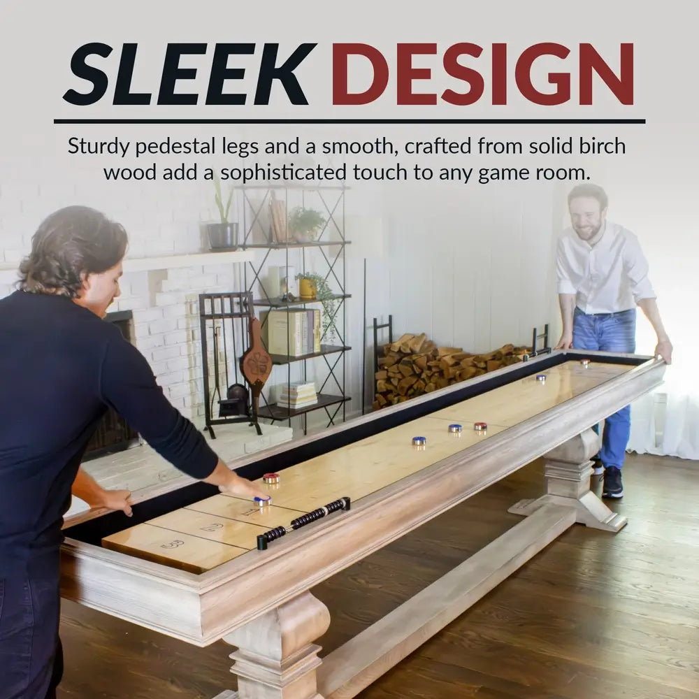 Two people playing on the Hathaway Montecito 12-ft Shuffleboard Table – Driftwood in a modern home game room, showing stylish pedestal base and elegant woodgrain finish.