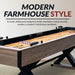 Side angle of the Excalibur shuffleboard table showing its modern farmhouse design with rustic driftwood melamine finish and black metal accents.