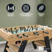 Foosball table in light oak finish with black-and-white players, red ball in ball return slot, and feature icons showcasing easy-grip handles, durable build, smooth gameplay, and 180-day limited warranty.