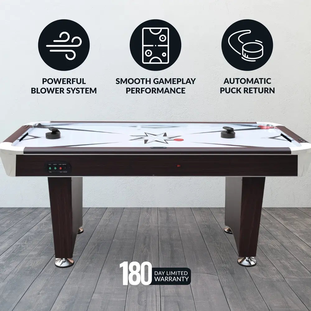 Side view of Hathaway air hockey table on a gray wood floor with icons showcasing powerful blower system, smooth gameplay performance, and automatic puck return. Includes 180-day limited warranty badge. Features black pushers, red pucks, and central star graphic.