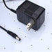 Air hockey table power adapter featuring a black AC wall plug with attached DC barrel connector. Shown resting on a white perforated playfield surface, used to power the table’s blower and electronic features.