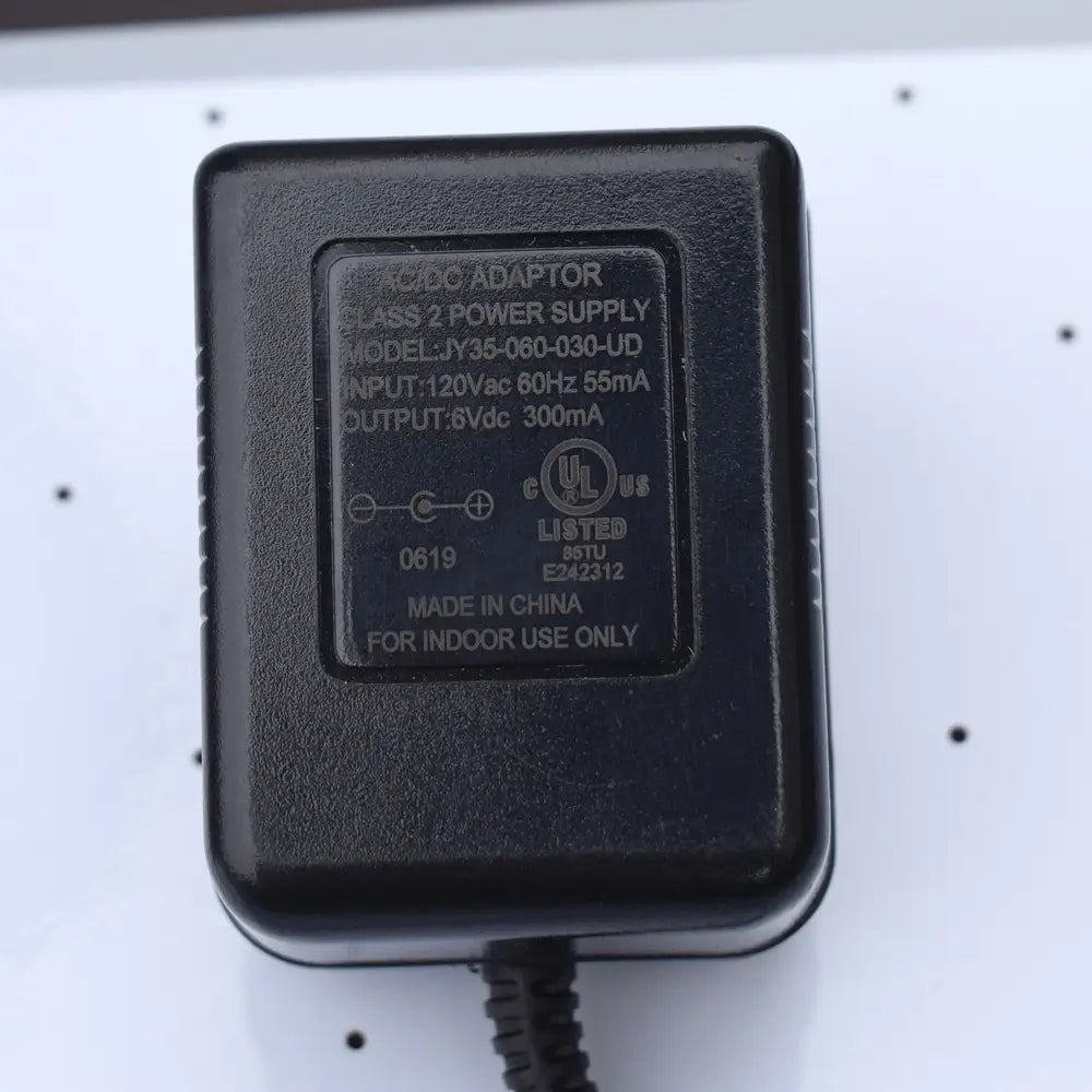 Close-up of label on Class 2 AC/DC power adapter for air hockey tables. Model JY35-060-030-UD with input 120V AC 60Hz 55mA and output 6V DC 300mA. UL-listed adapter, marked “For indoor use only,” shown on air hockey table surface.