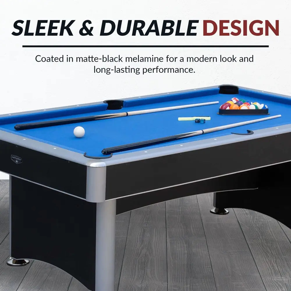 Hathaway pool table with blue felt and matte black melamine coating, displayed in a modern room setting with included accessories like cue sticks, chalk, and racked billiard balls.