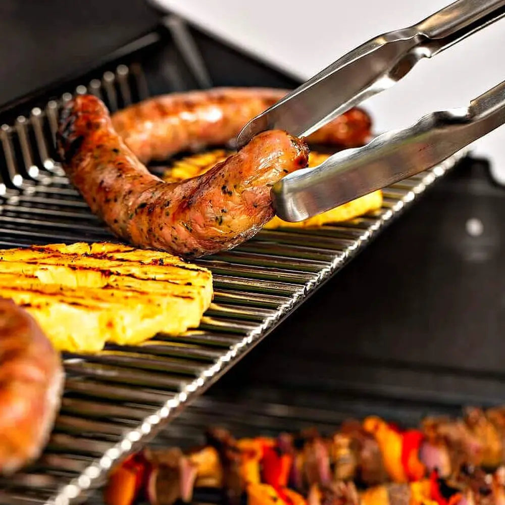 Heavy-duty stainless steel warming rack inside a Broil King grill holding grilled sausages, pineapple, and vegetable skewers.