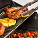 Heavy-duty stainless steel warming rack inside a Broil King grill holding grilled sausages, pineapple, and vegetable skewers.
