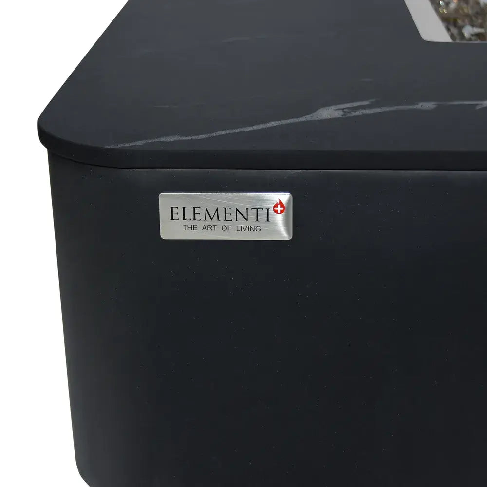 Close-up of the silver Elementi "The Art of Living" brand logo plaque on a black porcelain fire table.