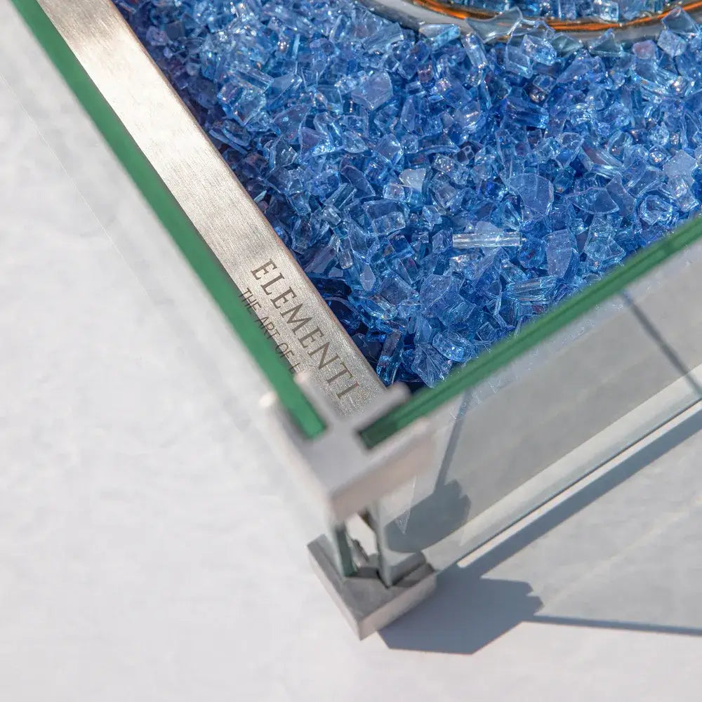 Macro shot of cobalt blue crushed fire glass and the branded Elementi stainless steel wind guard corner.