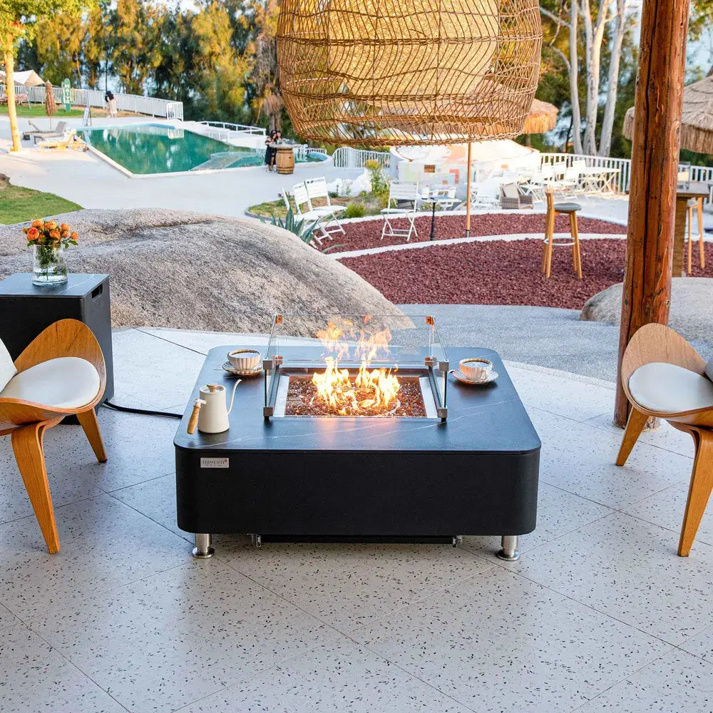 p	Luxury backyard patio featuring the Elementi porcelain fire table with glass wind guard overlooking a swimming pool.
