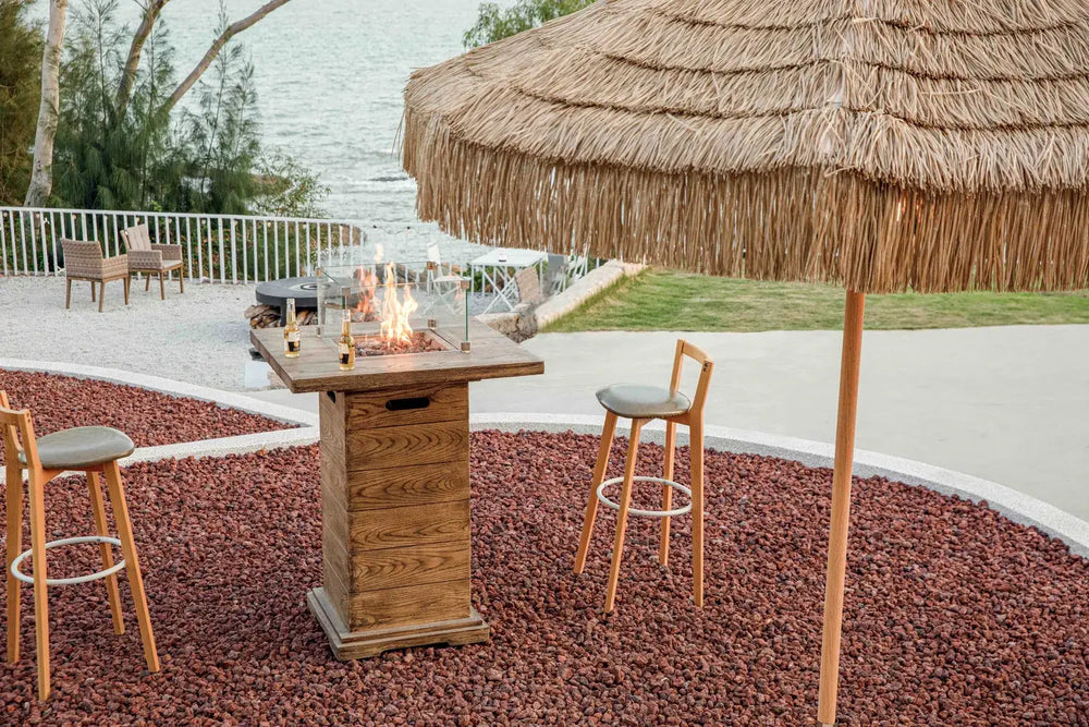 Lit Elementi OFG224 Rova Fire Bar Table 40k BTU on a coastal balcony during sunset with atmospheric lighting.