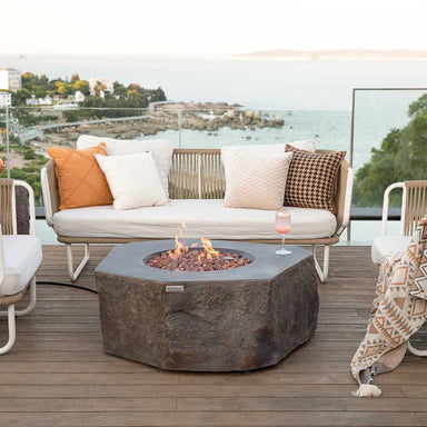 Luxury outdoor patio setup featuring the Elementi Columbia fire table on a wooden deck with modern sofa seating and a coastal view.