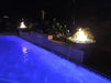 Pair of Travertine TessaRai fire and water bowls glowing at night above blue-lit swimming pool with waterfall streams
