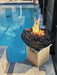 Black Travertine TessaRai fire and water bowl on pool pedestal with bright flames and modern backyard pool.
