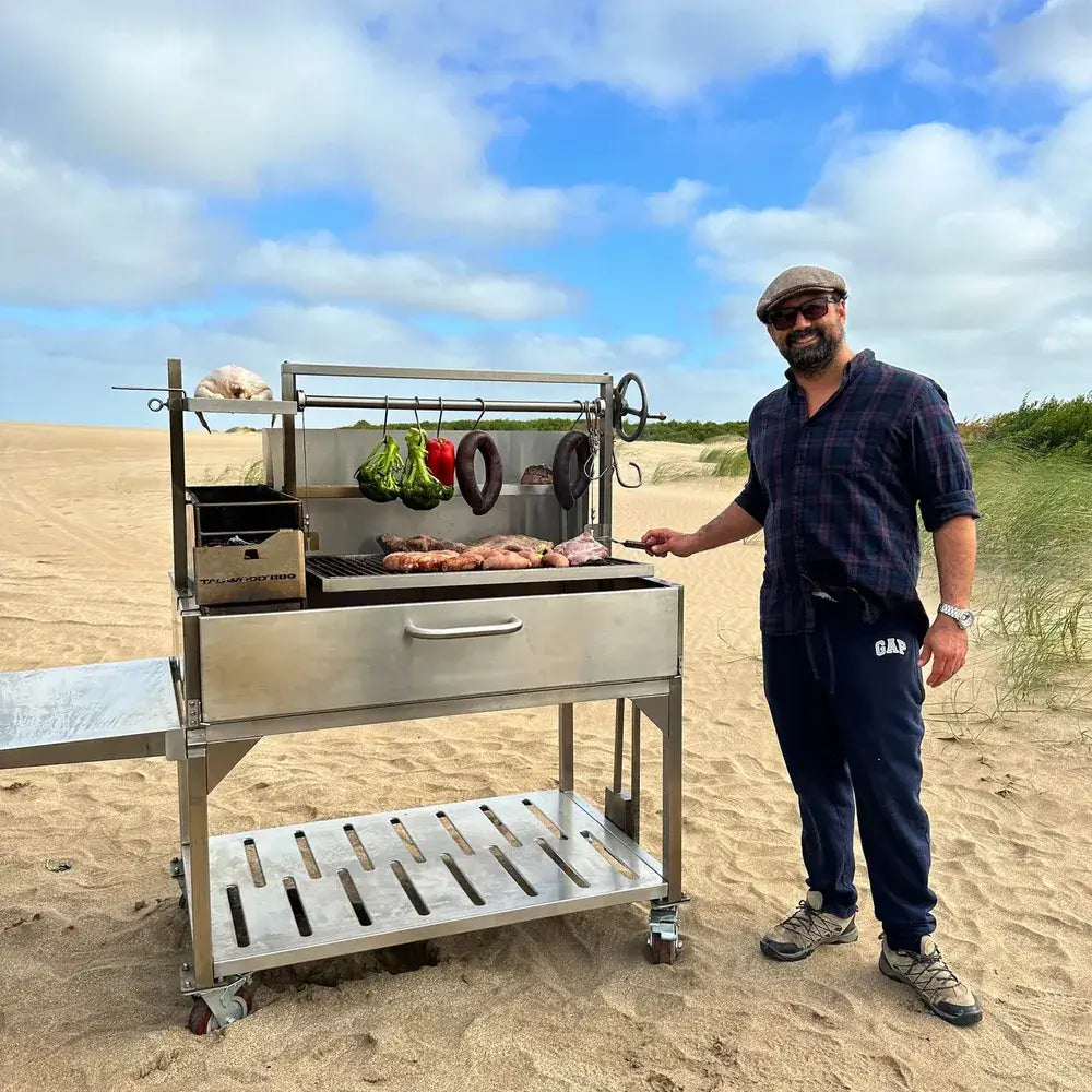Tagwood BBQ23SS XL Santa Maria grill cooking meats on beach with chef beside grill