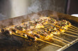 Meat and vegetable skewers sizzling on outdoor stainless steel flat top griddle