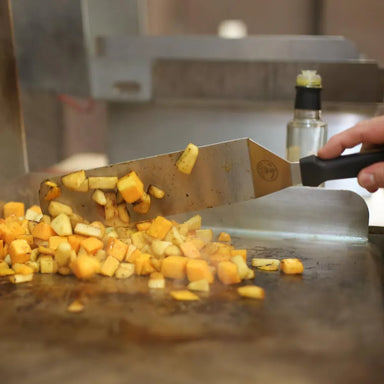 Le Griddle Accessory Kit tools next to chopped vegetables and food cooking on the flat-top griddle.