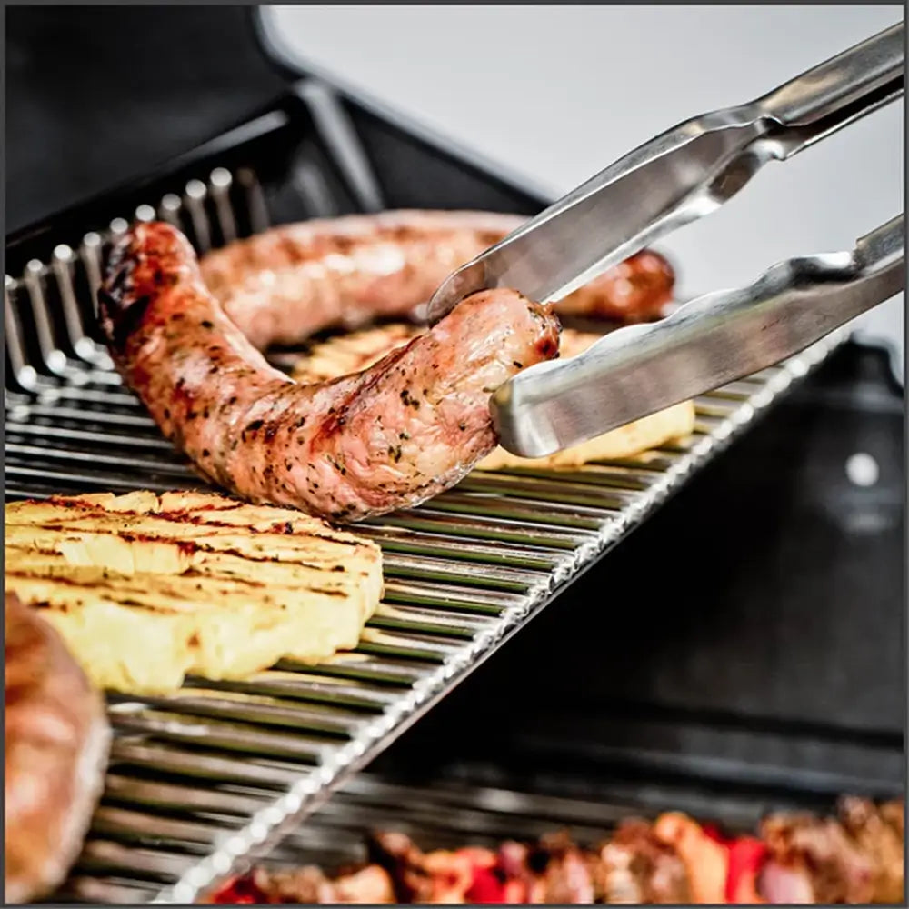 Sausage and pineapple slices grilling on the stainless steel warming rack of a Broil King gas grill.