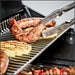 Sausage and pineapple slices grilling on the stainless steel warming rack of a Broil King gas grill.